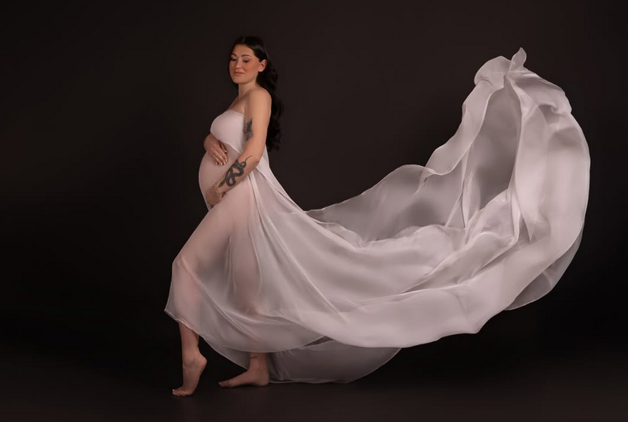 Babybauch-Shooting mit fließendem Tuch vor dunklem Hintergrund